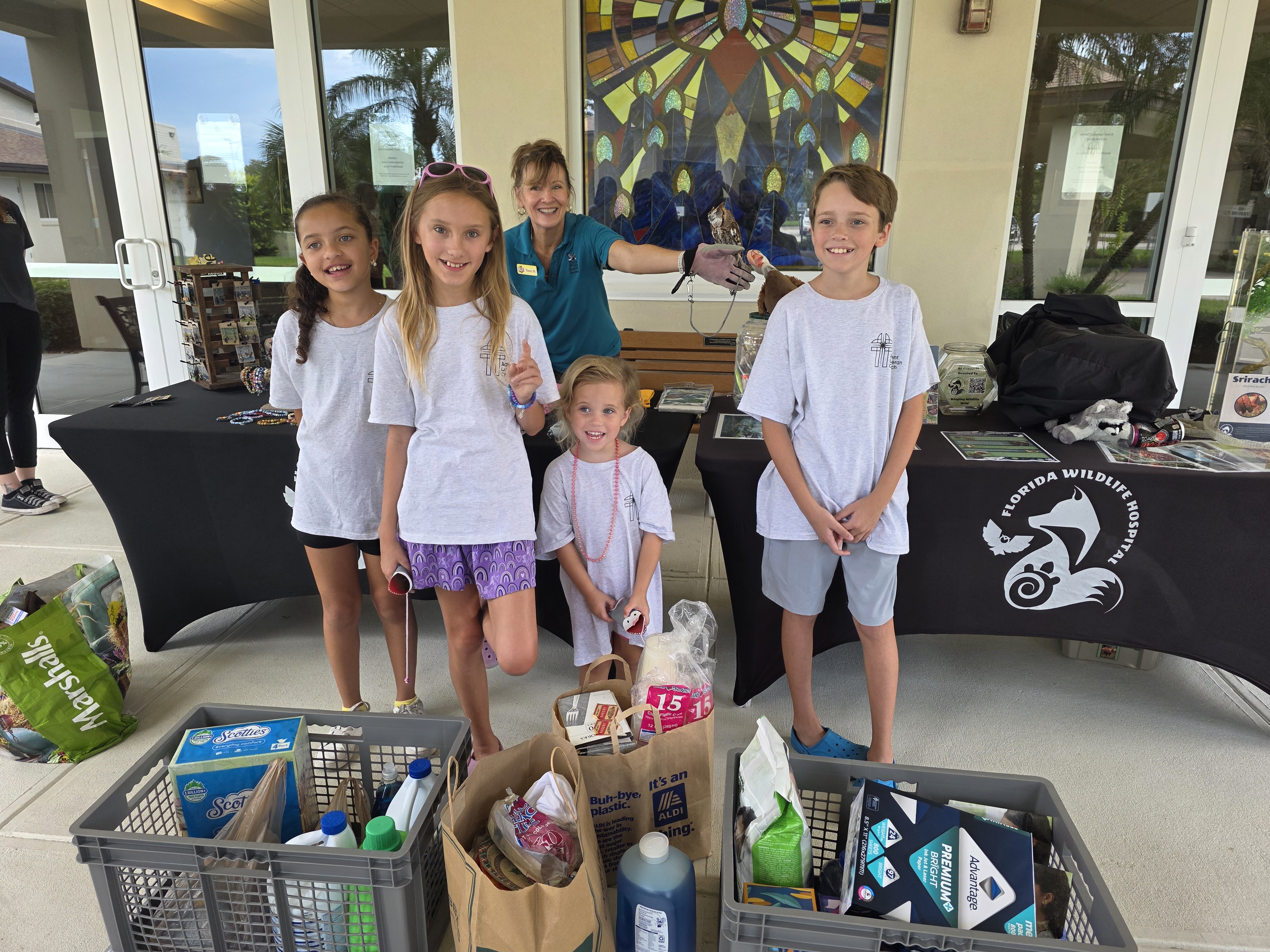 kids with the donations and the fwh representative holding an owl, smiling at the camera